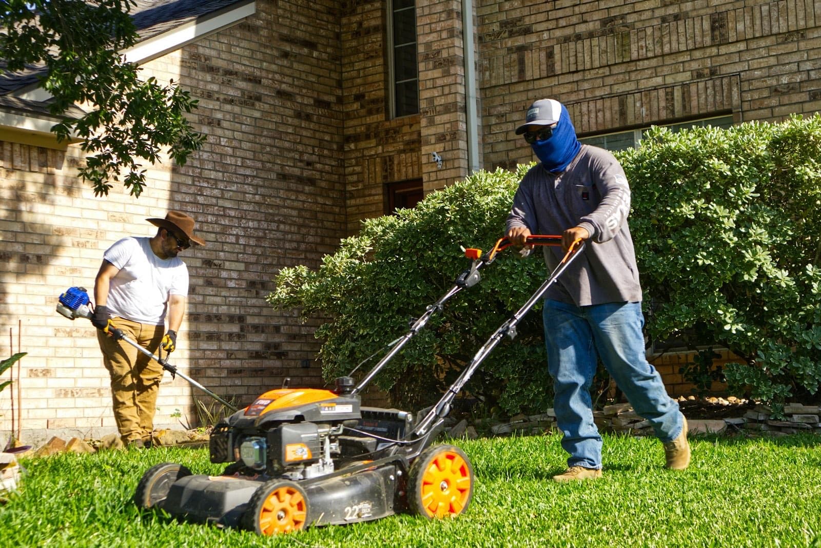 A two-person crew mowing and trimming a residential lawn